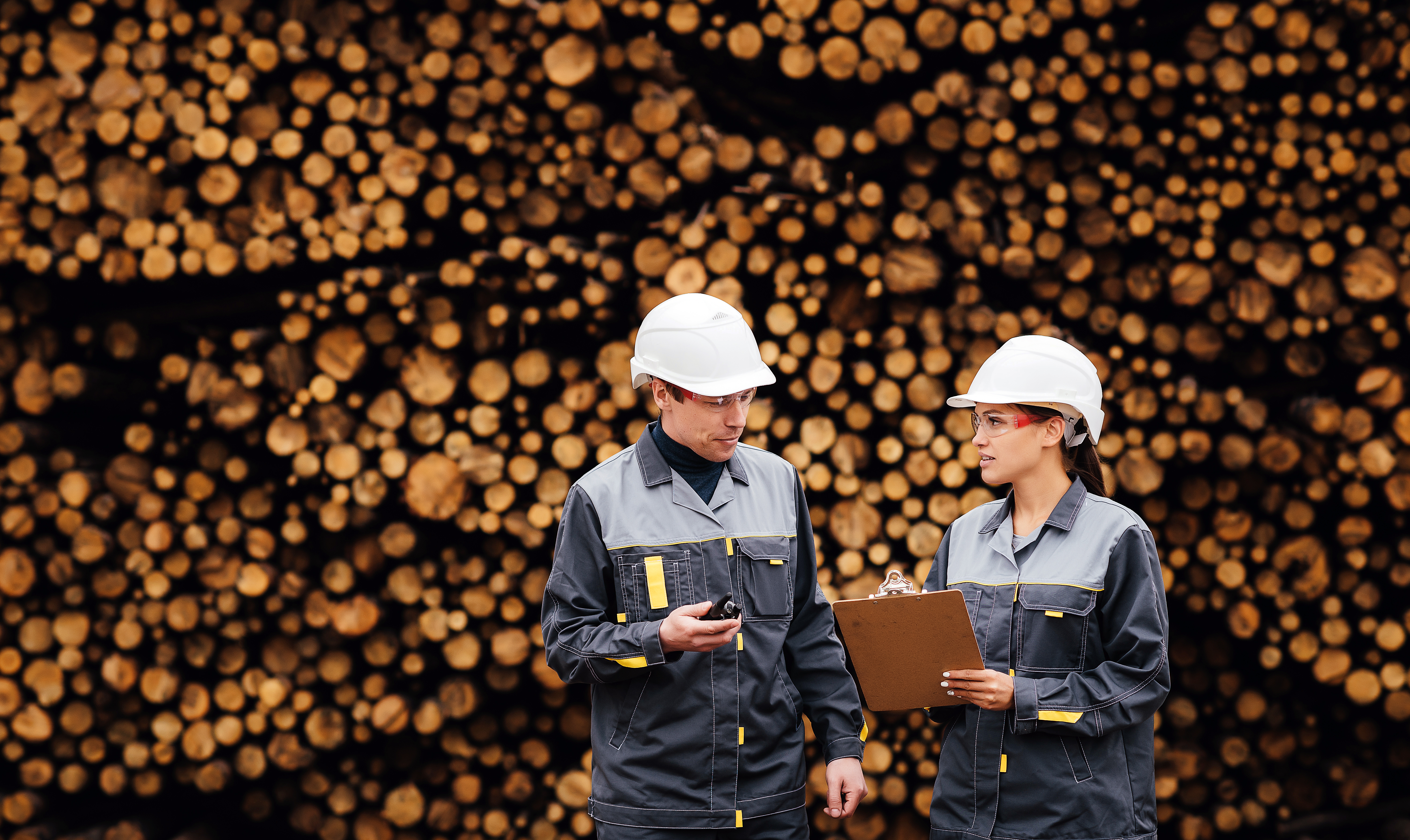 Man och kvinna med hjälmar står framför virke, pratar och tittar på ett papper