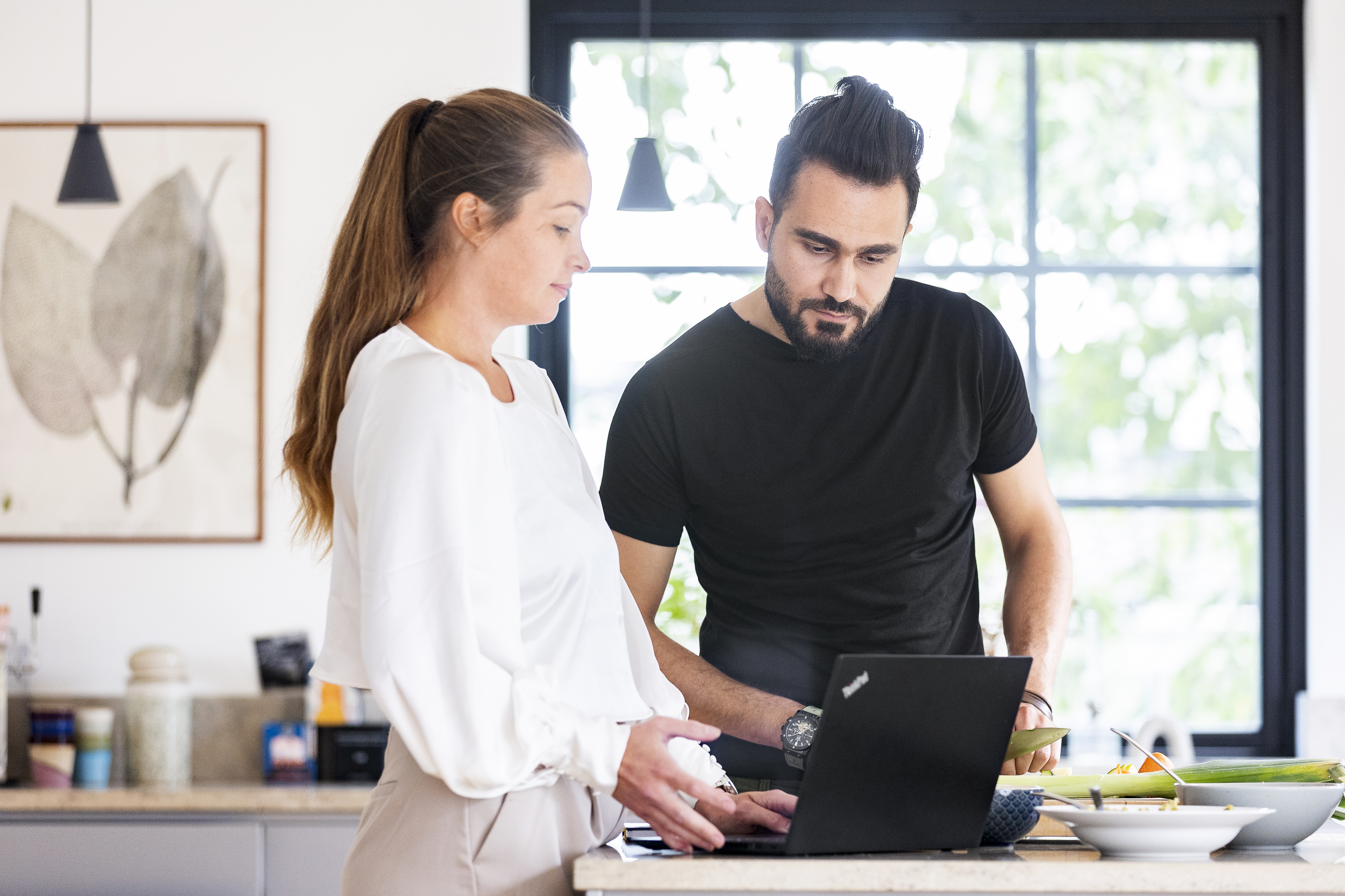 “Två personer står i ett ljust rum och tittar koncentrerat på en bärbar dator. Den ena personen håller datorn medan den andra pekar mot skärmen.”