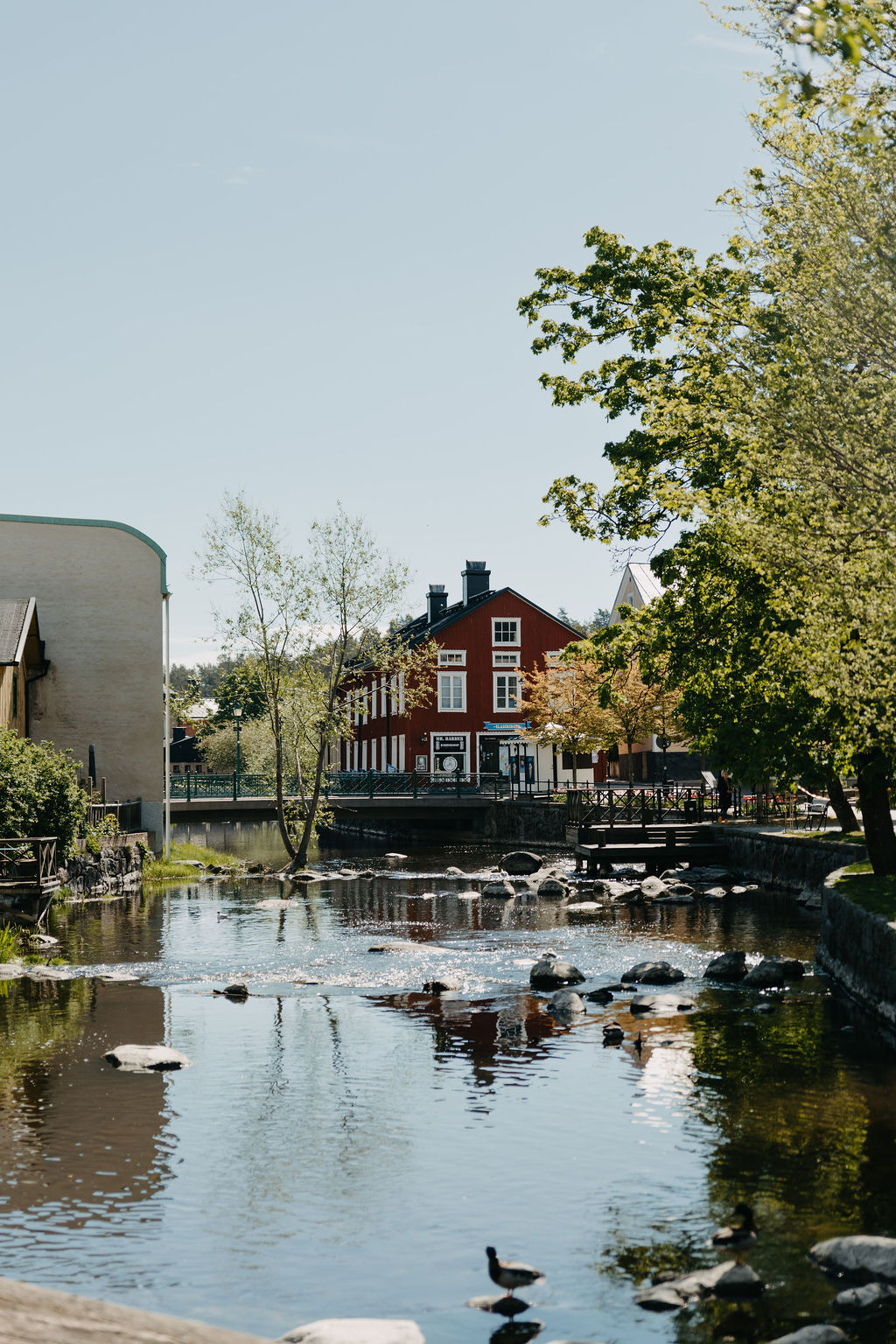 Å som flyter genom en grönskande stadsmiljö med träd, stenar och röda byggnader i bakgrunden