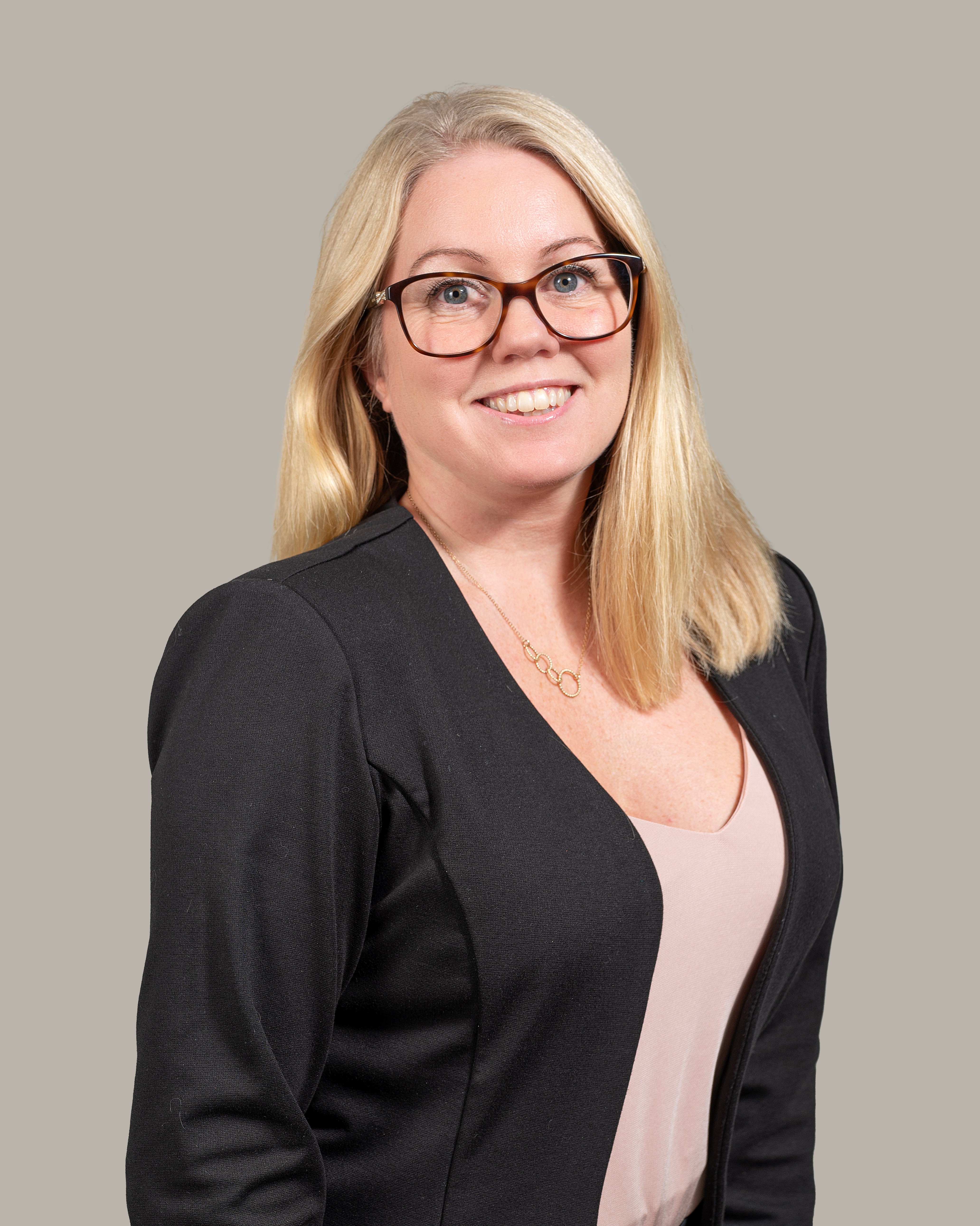 Porträtt av en leende premiumrådgivare med axellångt blont hår, glasögon och svart kavaj mot en neutral bakgrund.